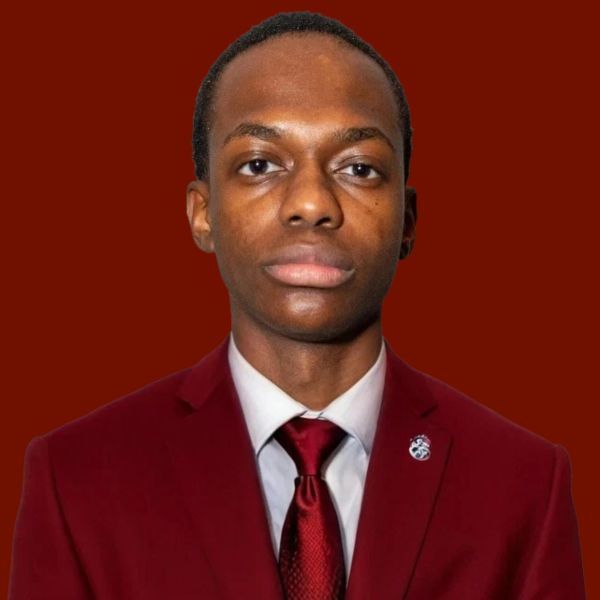 Young Black man in a red suit and tie, professional headshot with a burgundy background.