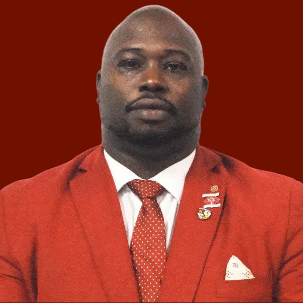 A Black man in a red suit and tie against a red background.