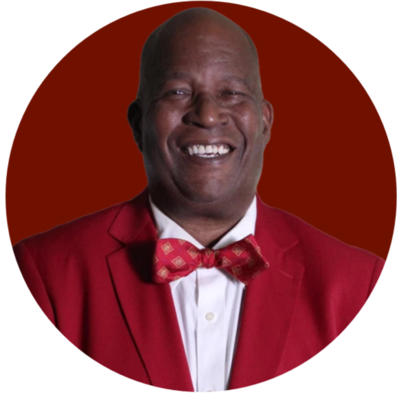 Smiling man in a red suit and bow tie with Western Province Greek fraternity emblem.