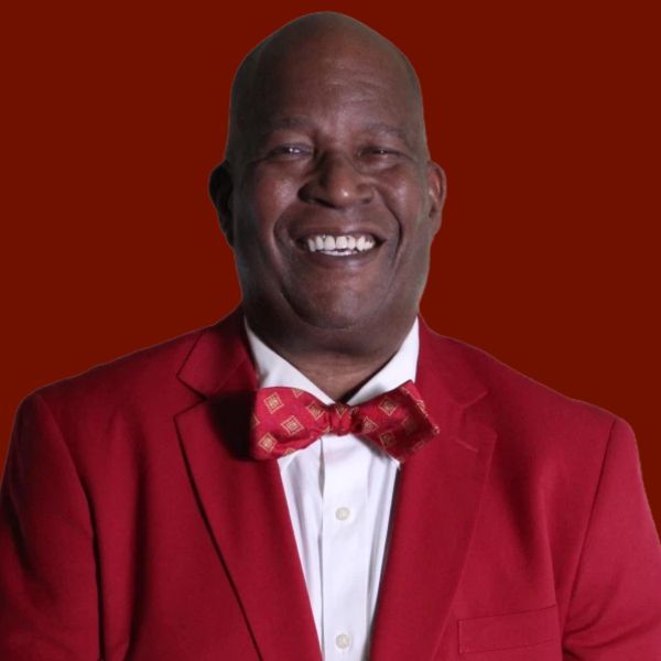 Smiling Black man in a red suit and bow tie, against a red background.