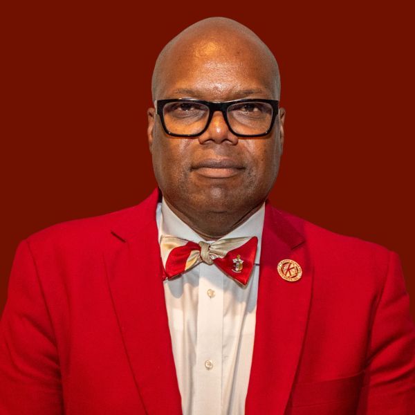 Man in a red suit, glasses, and bowtie, on a red background.
