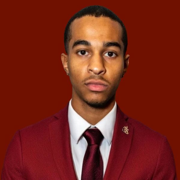 Young Black man in maroon suit and tie, serious expression.