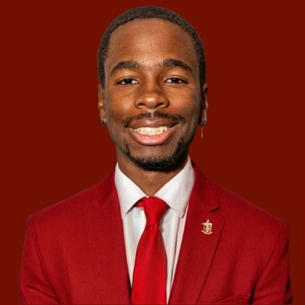 Young Black man in a red suit and tie, smiling, against a burgundy background.