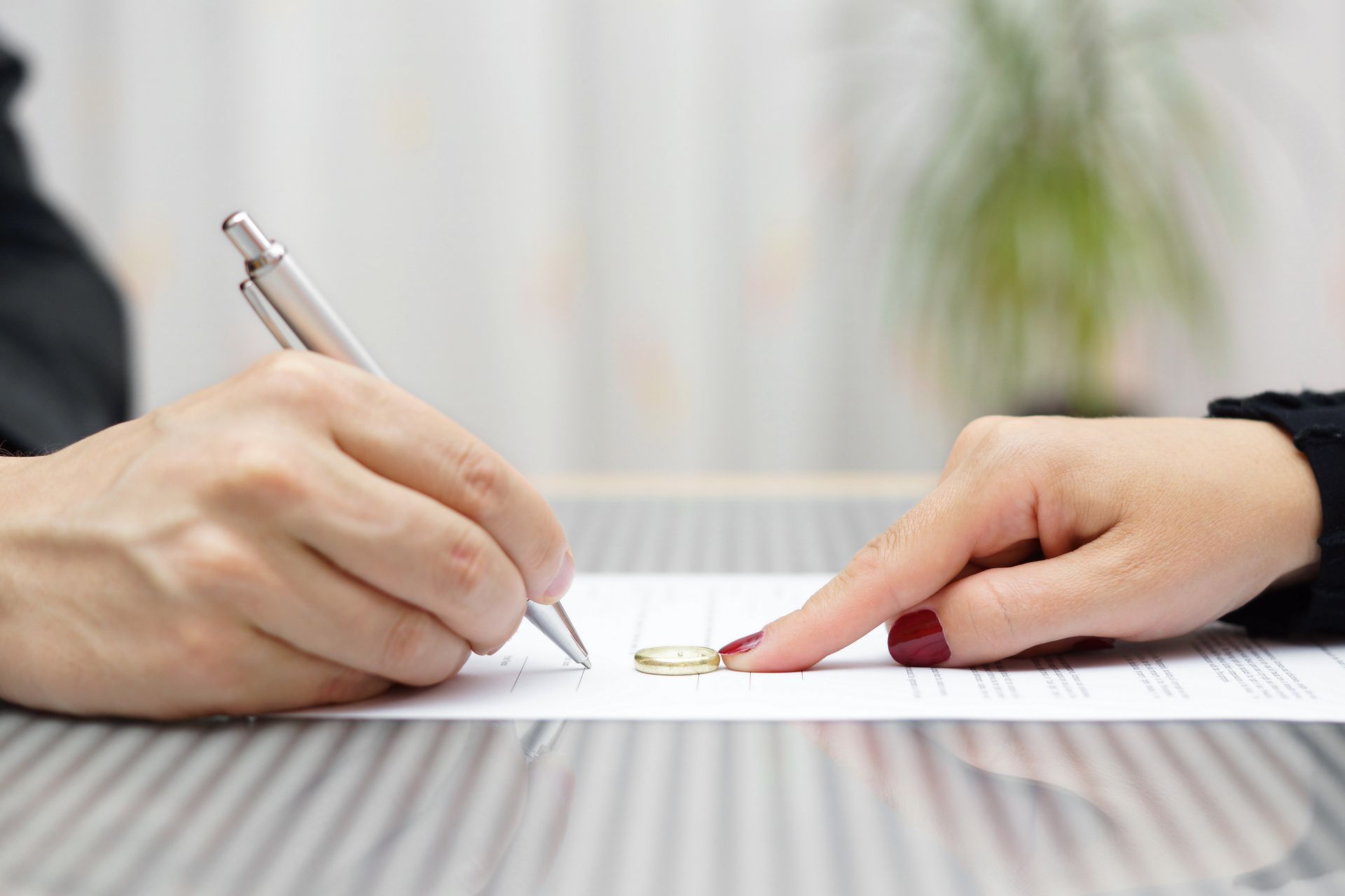 Hands signing a document; a wedding ring lies on the paper.