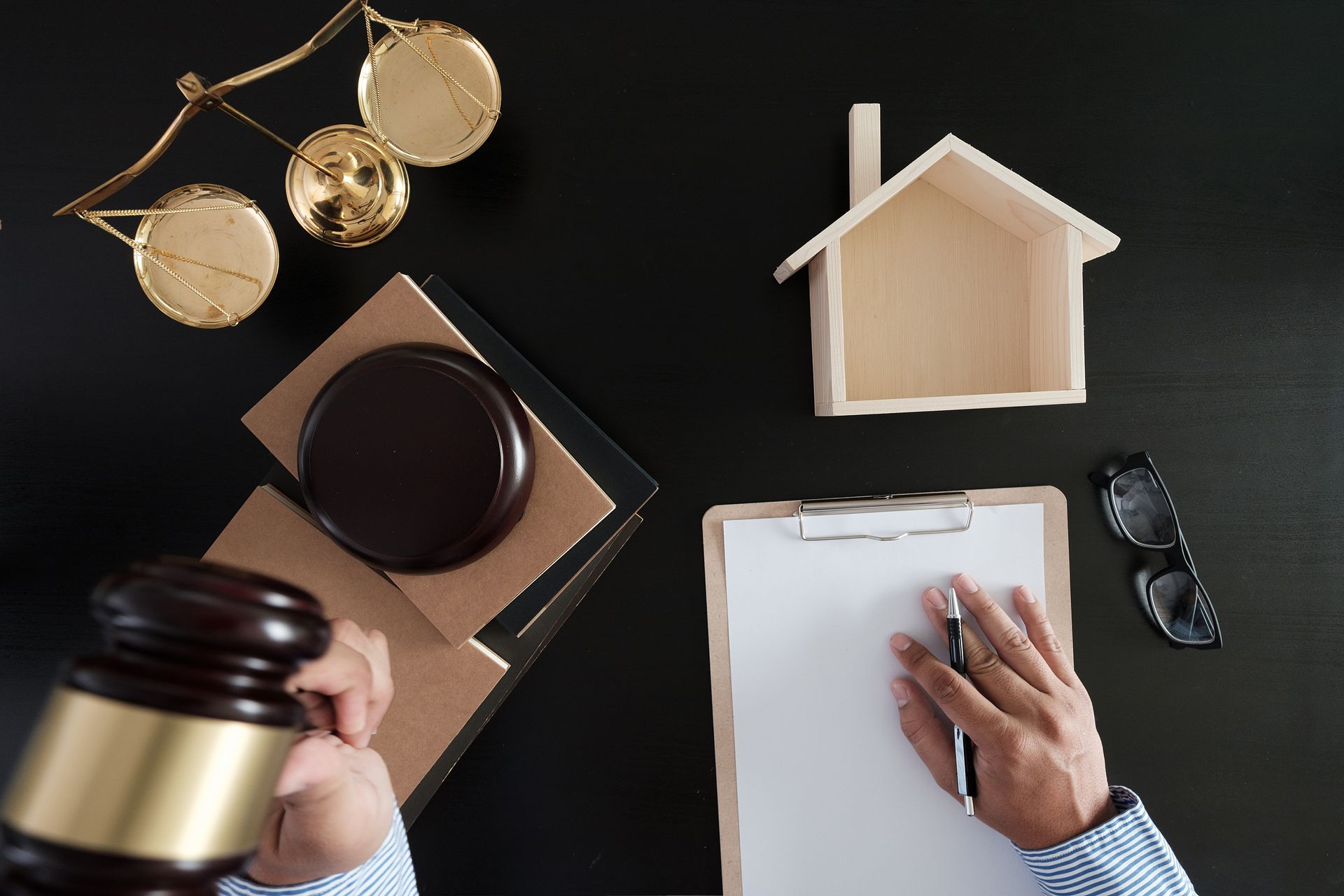 Hand with gavel next to scales of justice, house model, and document on a table.