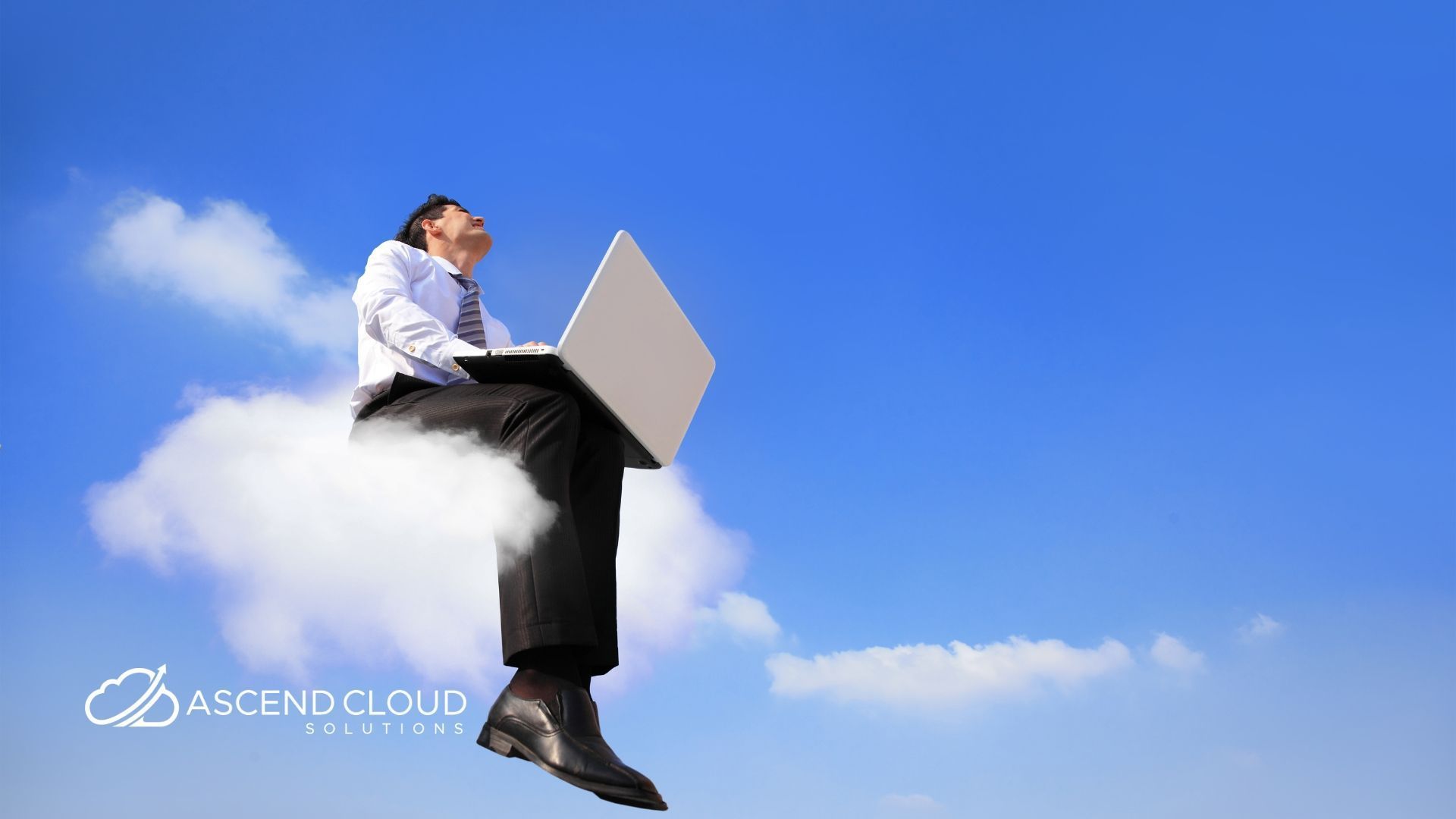 A man is sitting on a cloud using a laptop computer.