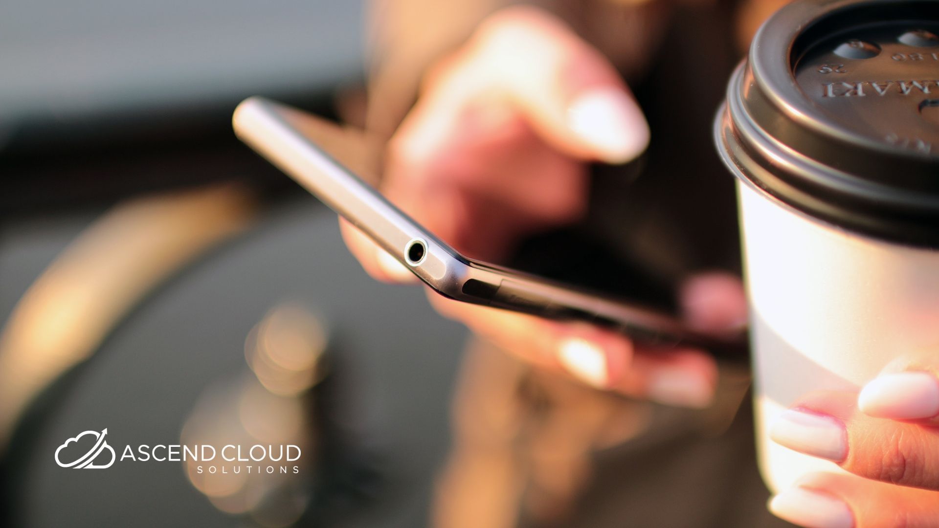 A person is holding a cup of coffee and using a cell phone.