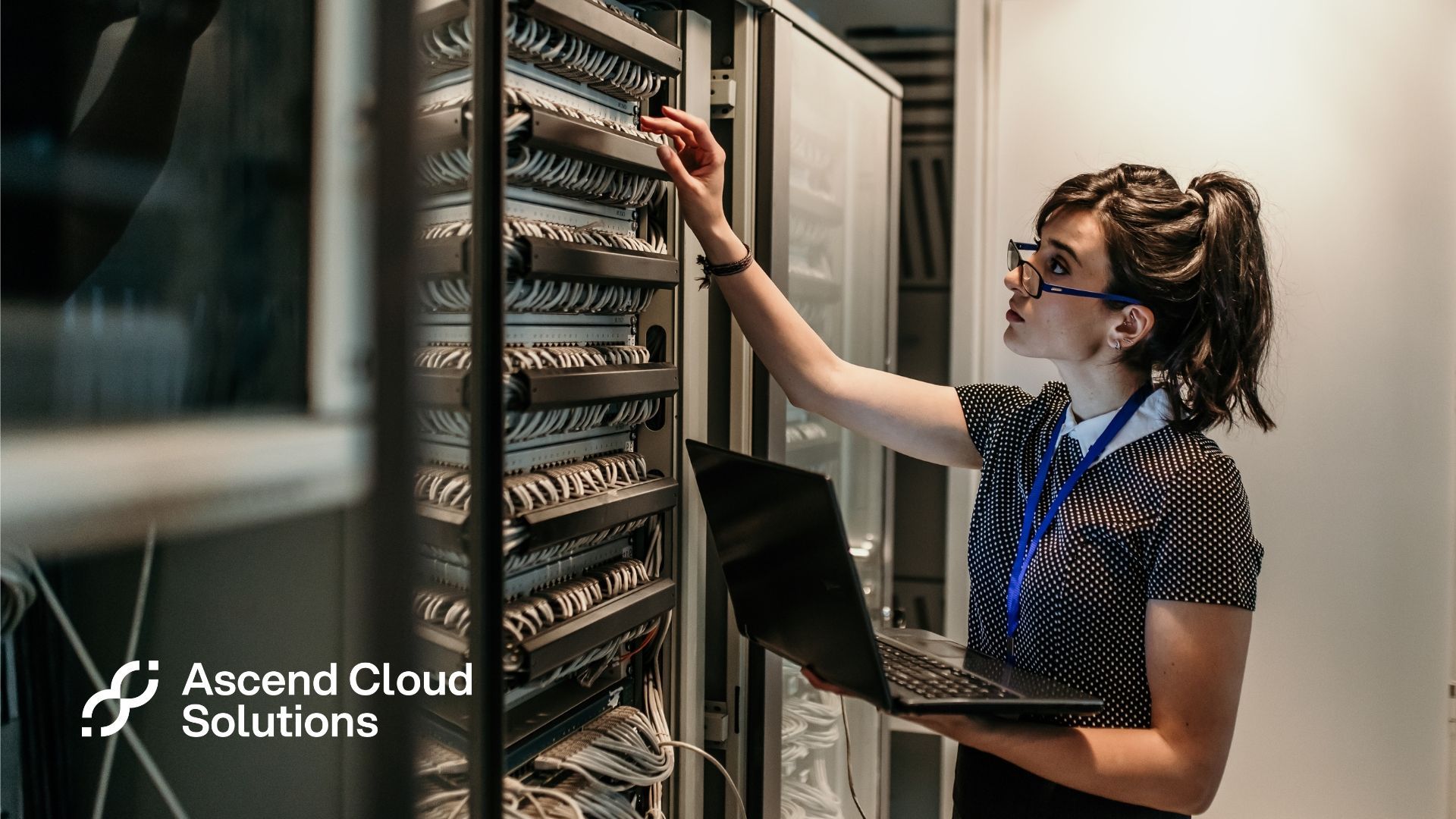 A woman is working on a server in a data center while holding a laptop.