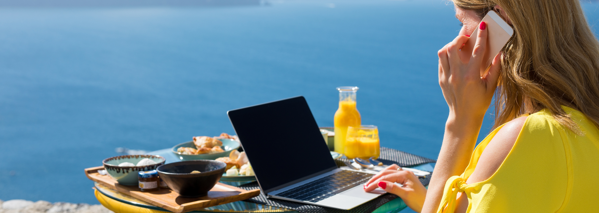 A woman is sitting at a table with a laptop and talking on a cell phone.