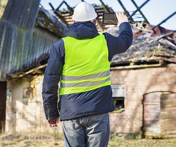 back of construction manager holding tablet and looking at dilapidated building