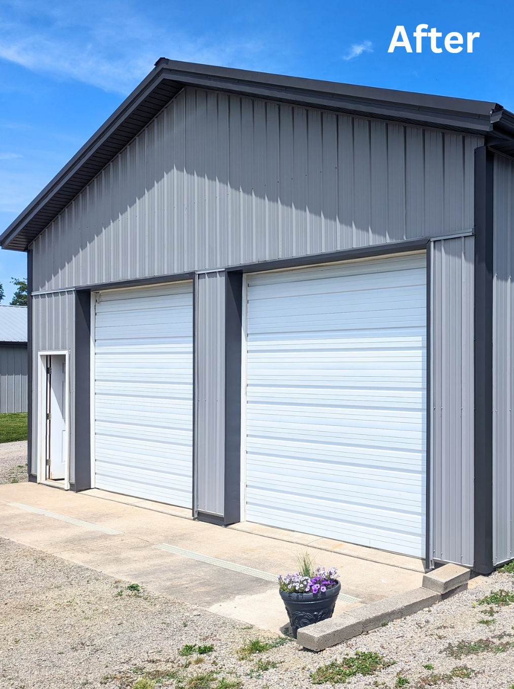 Gray metal garage with two white roll-up doors and a small potted flower on the concrete pad.