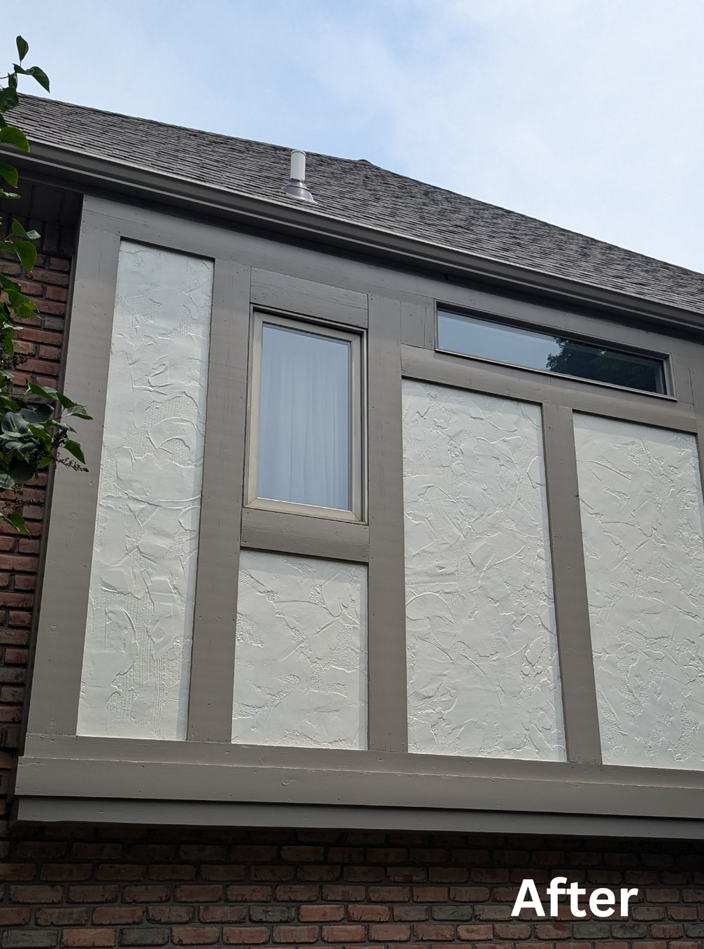Renovated house exterior with gray stucco panels, a small window, and a brick lower wall under a tiled roof