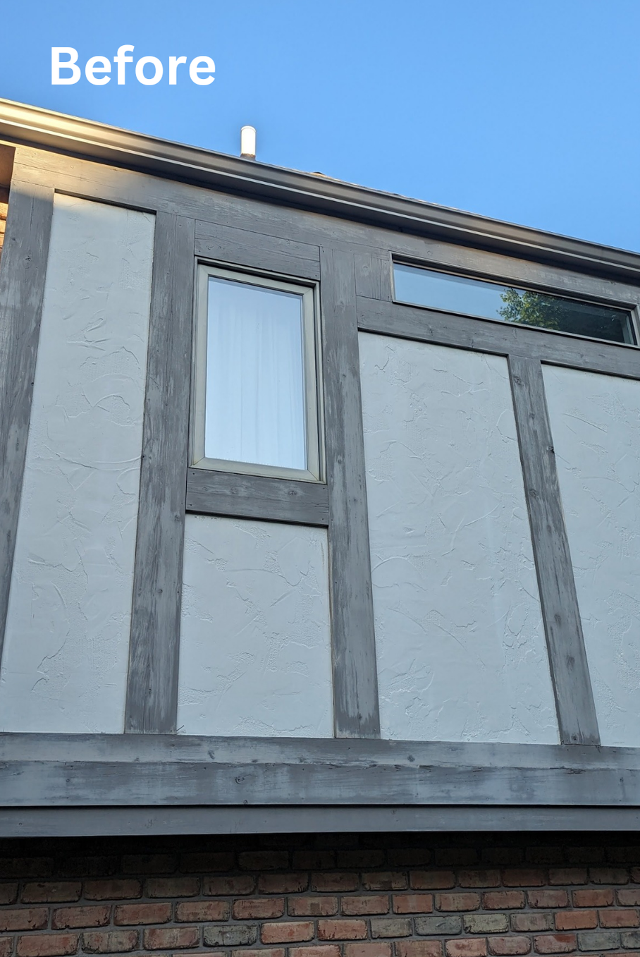 Before photo of a house exterior with gray paneling, a window, and brick at the bottom under blue sky