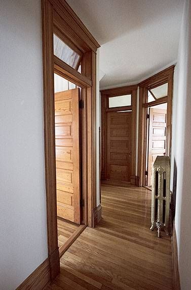 Narrow hallway with wooden doors, herringbone floor, and a radiator at the far end