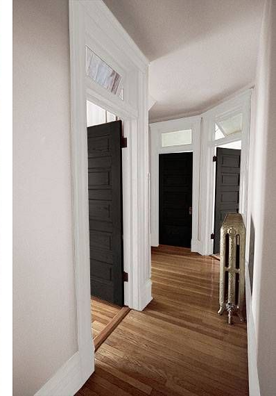 Narrow white hallway with dark doors, hardwood floors, and a radiator near a bright window.
