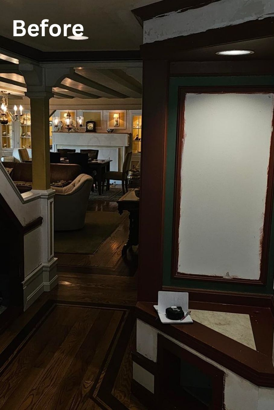 Before view of a dim hallway opening into a cozy living room with a blank framed wall panel.