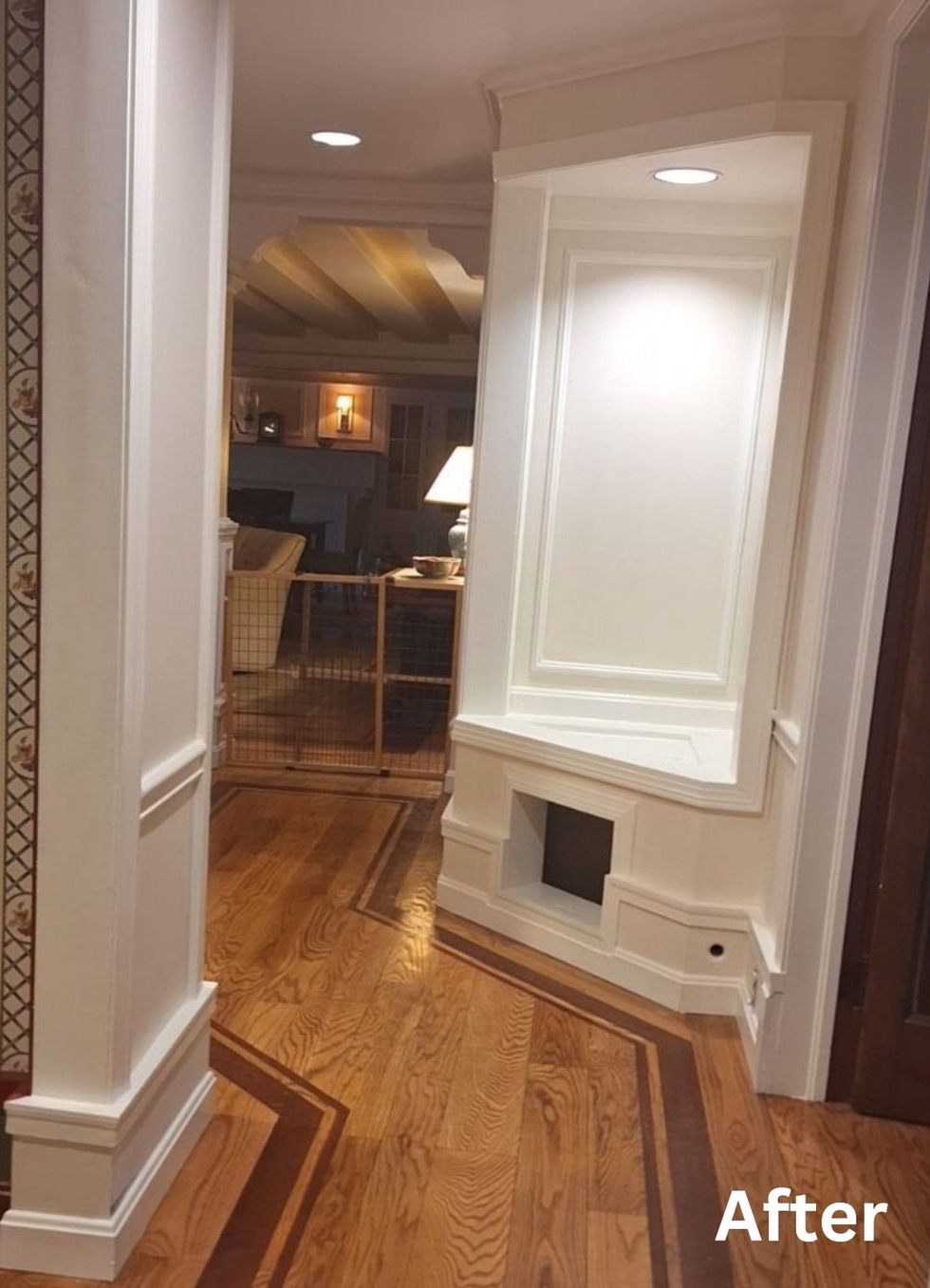 Hallway with white trim and wainscoting, leading to a warm kitchen or dining area with hardwood floors.