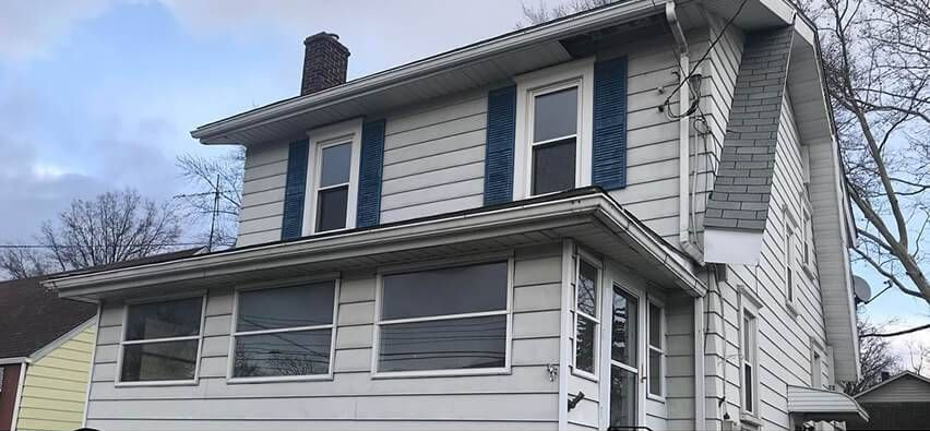 Two-story white house with blue shutters and enclosed porch on a cloudy day
