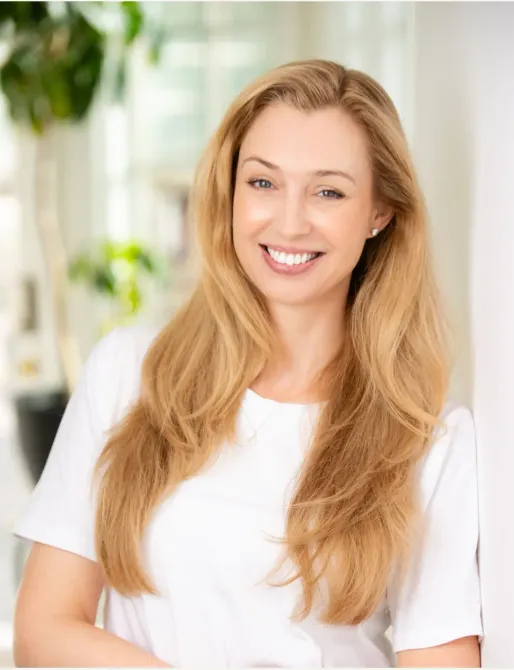 A woman with long blonde hair is wearing a white shirt and smiling.