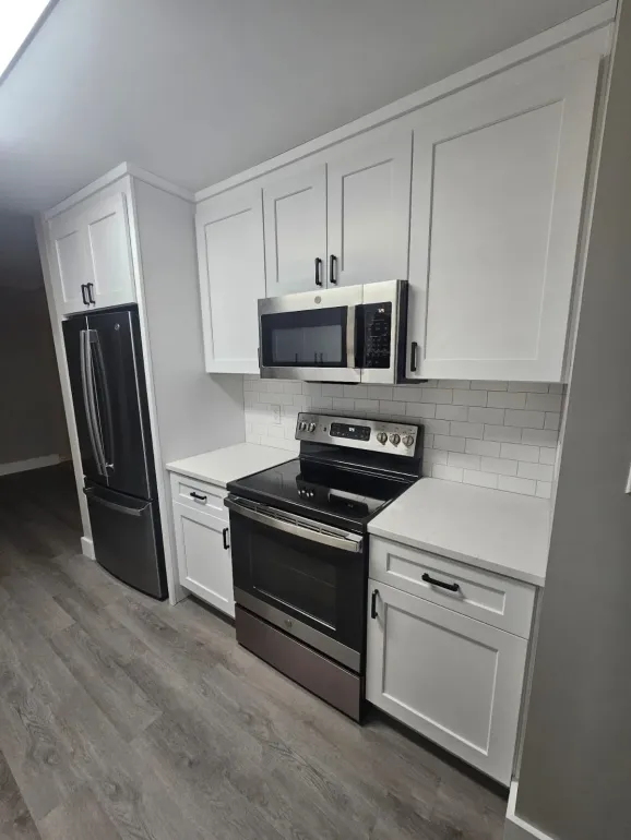 A kitchen with a stove , microwave , refrigerator and cabinets.