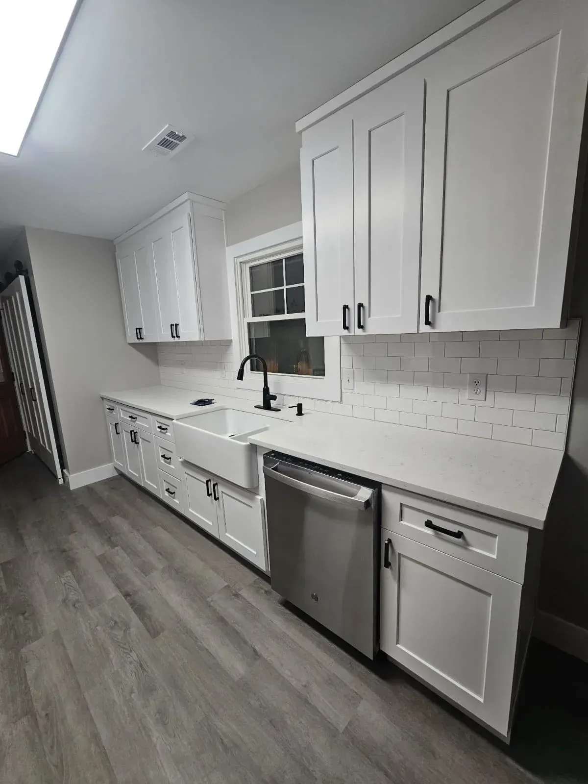 A kitchen with white cabinets , a sink , and a stainless steel dishwasher.