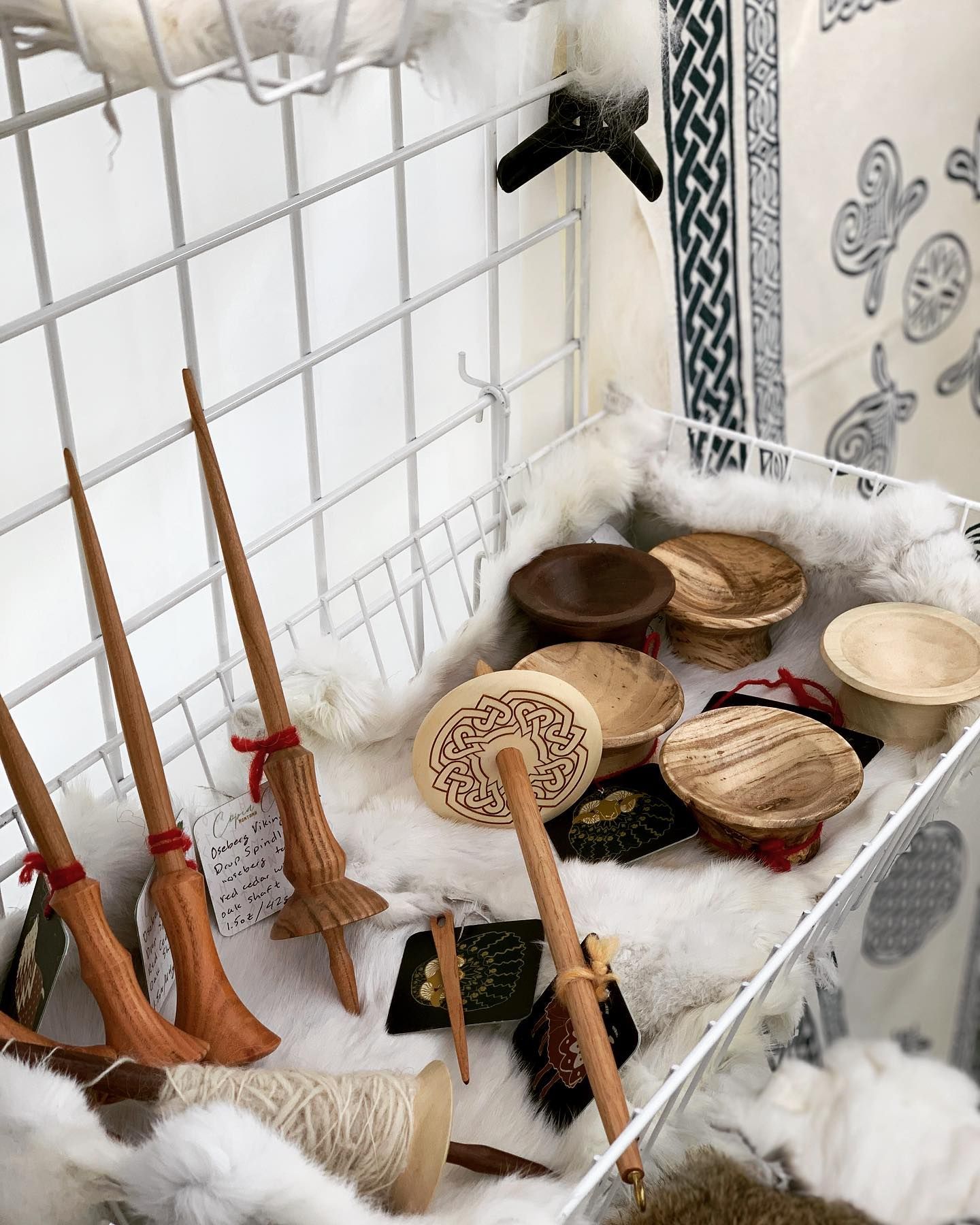 Spinning spindles and whorls displayed in a white wire basket with white fluffy material.