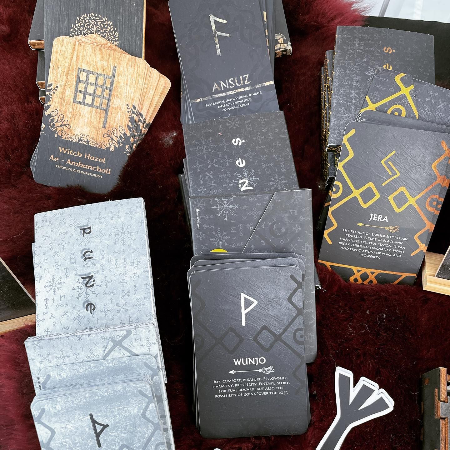 Close-up of rune cards, some fanned out. Gray, black, and gold cards with symbols, on red textured surface.