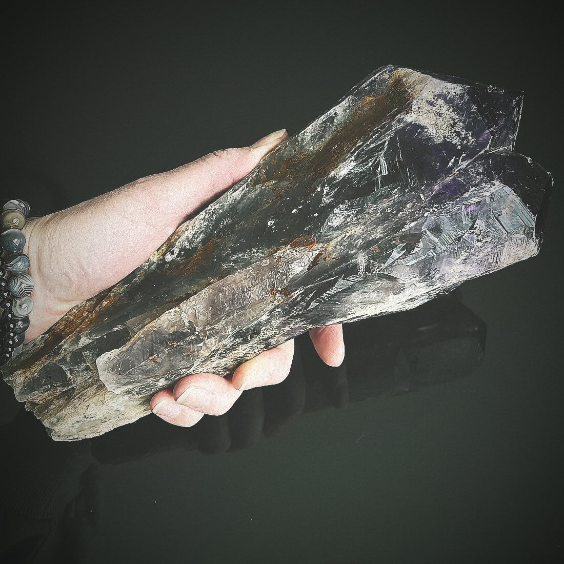 Hand holding a large, dark amethyst geode against a black background.
