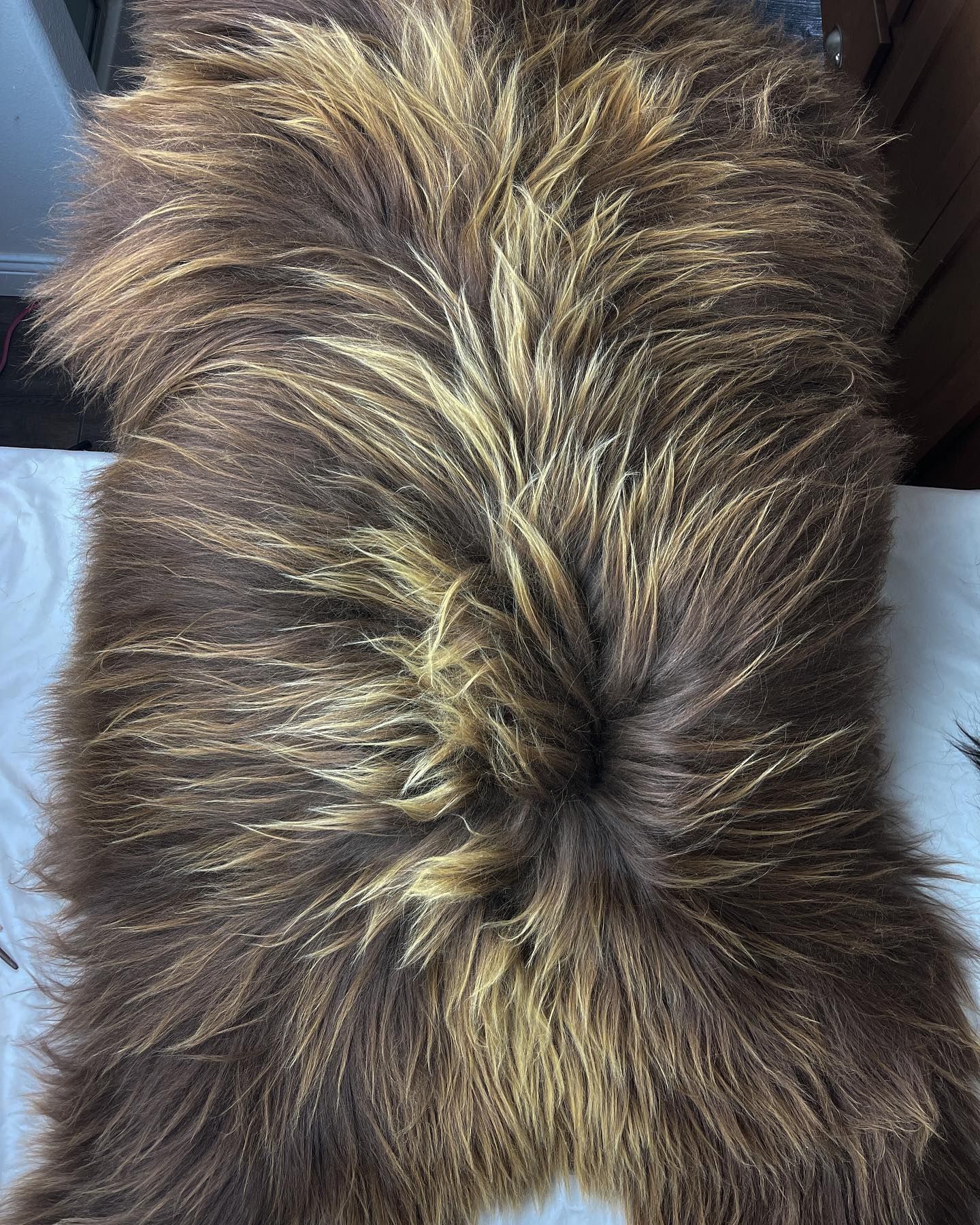 Brown and tan faux fur rug with a central swirl pattern, lying on a white surface.