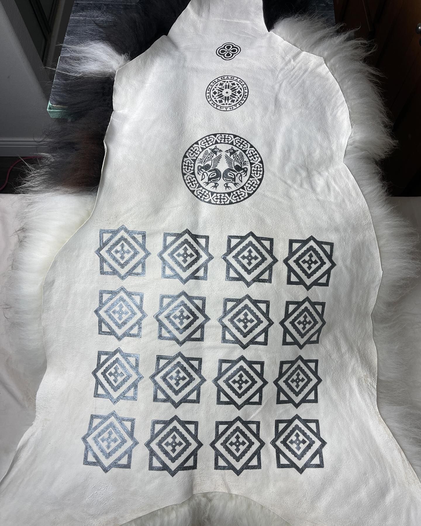 White textile with repeating geometric patterns and two circular emblem designs in gray.