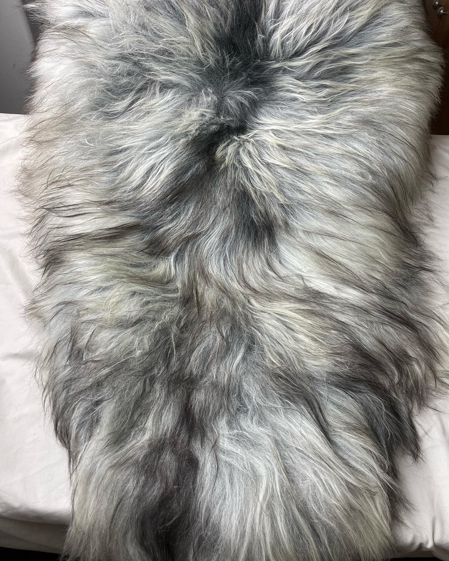 Gray and white faux fur rug, plush and textured, on a white surface.