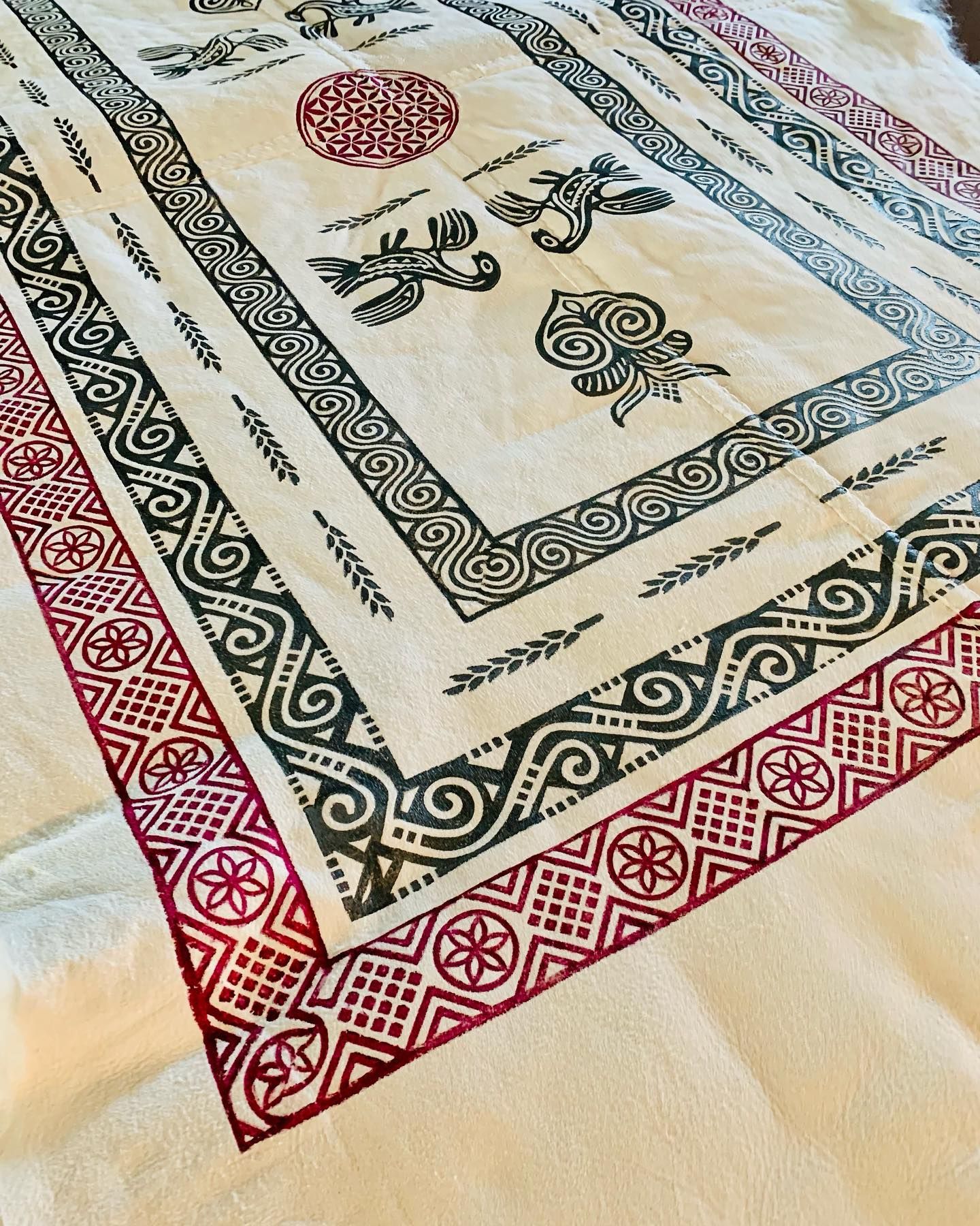Cream-colored fabric with dark green and red block-printed designs, including borders, medallions, and bird-like figures.