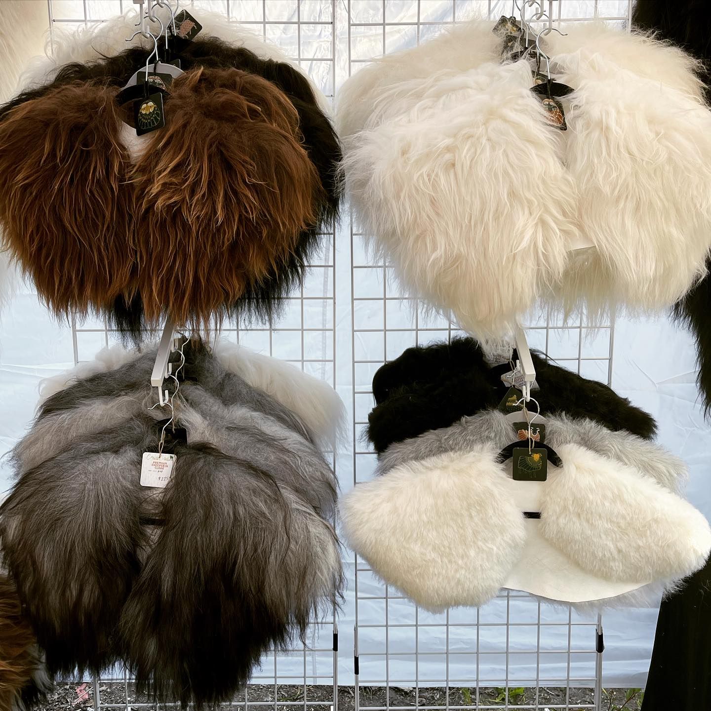 Four fluffy, shaggy fur collars in brown, white, gray, and black, hanging on a white grid display.