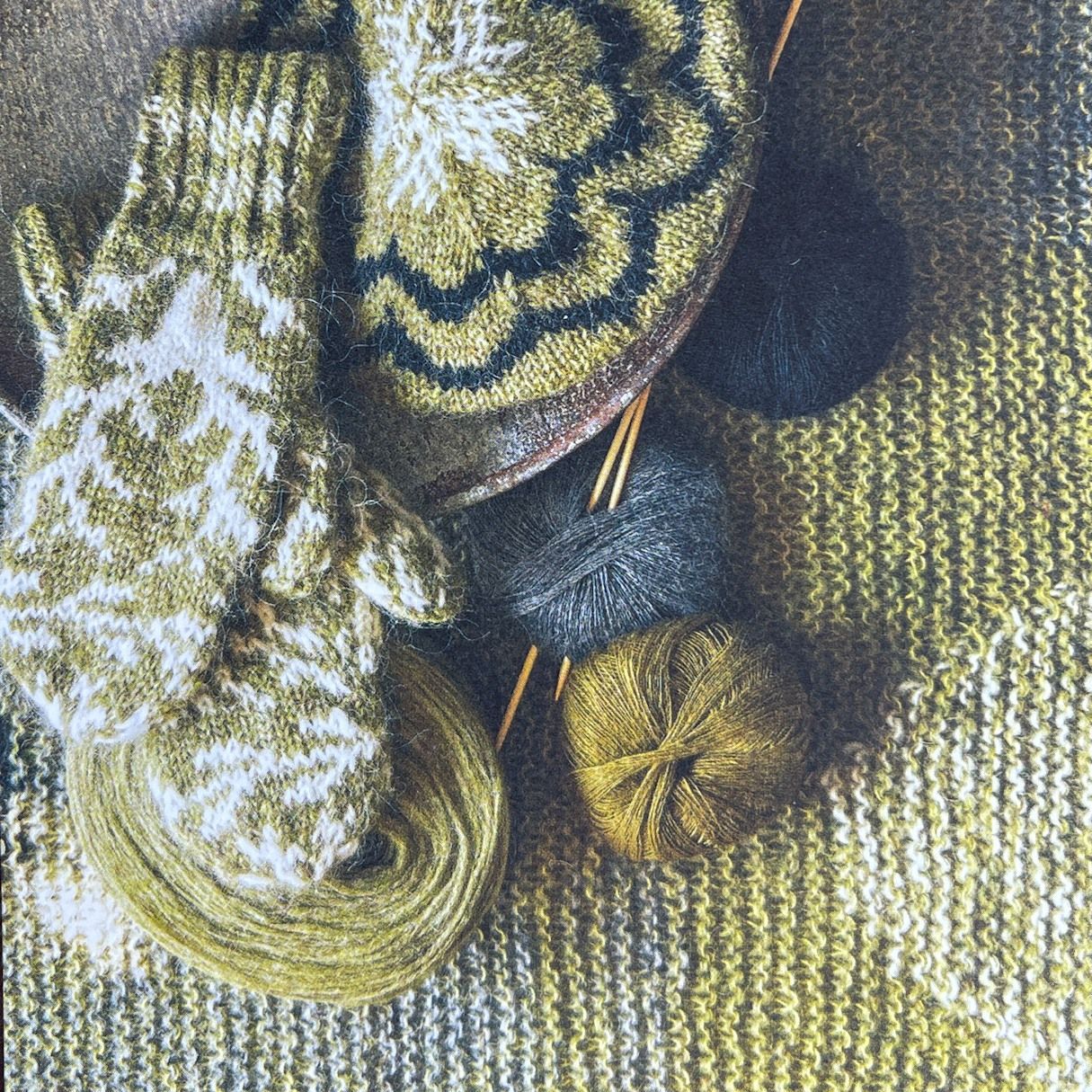 Cozy scene of knitted mittens, hat, yarn, and needles in shades of green, gold, and white.