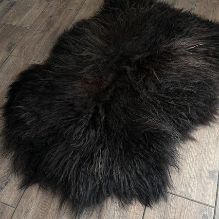 Black sheepskin rug on light wooden floor.