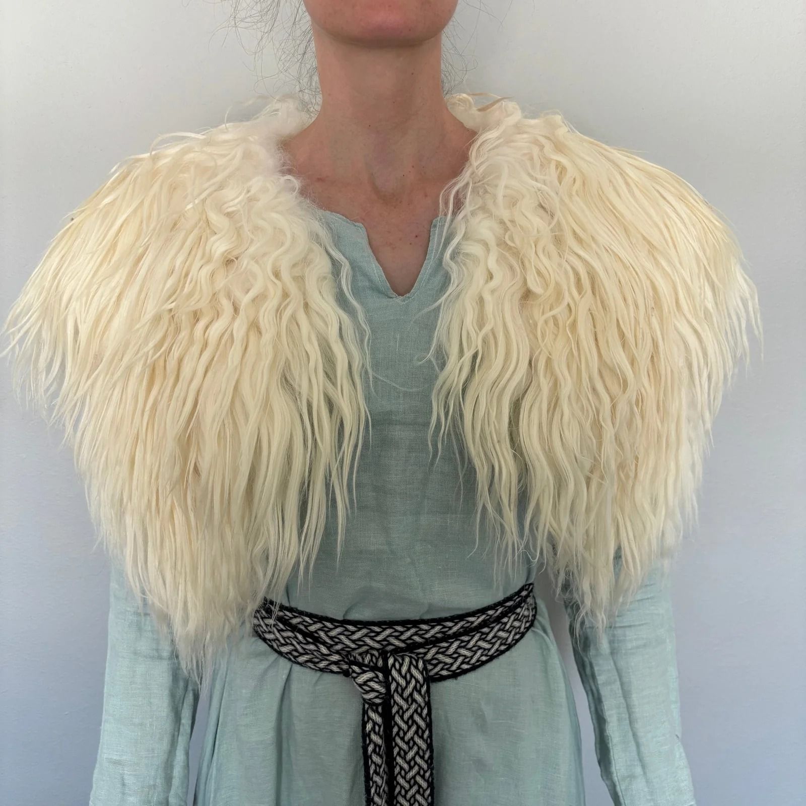 Woman wearing a light blue dress, a fuzzy white fur collar, and a woven black and white belt.