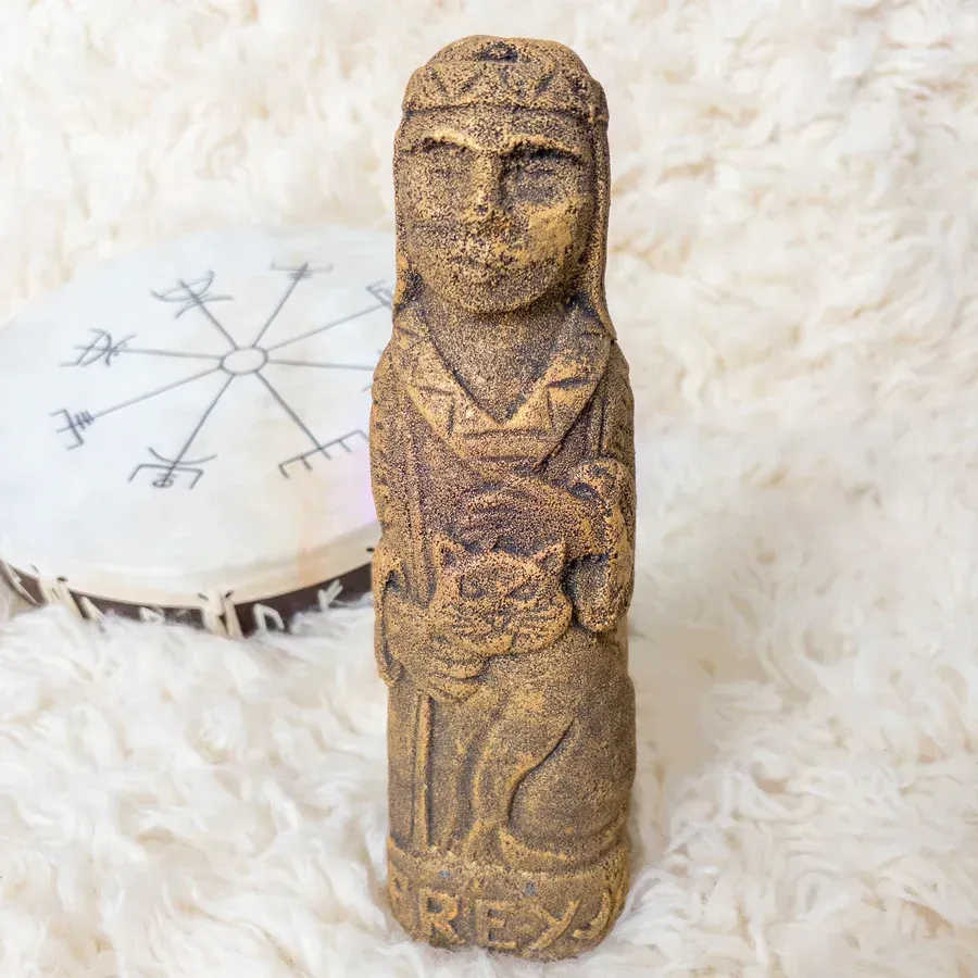 Stone statue of a woman with a cat, tan color. Beside a drum with runic symbols.