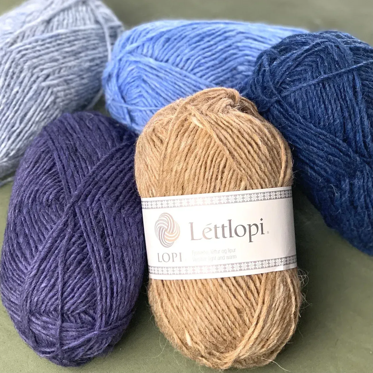 Skeins of blue, brown, and gray Icelandic wool yarn on a green surface. The yarn is Lèttlopi brand.