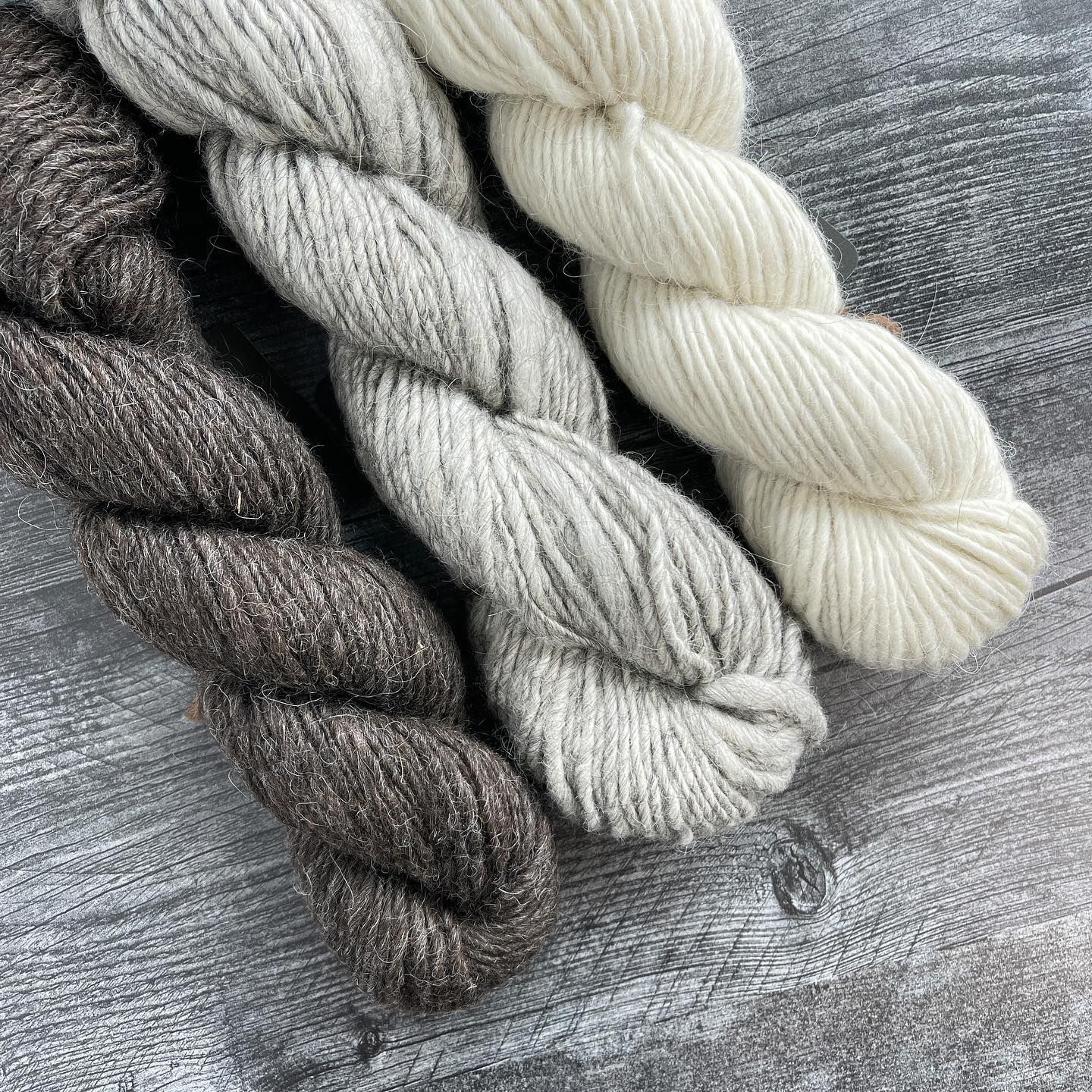 Three skeins of yarn in brown, silver, and white, twisted on a gray surface.