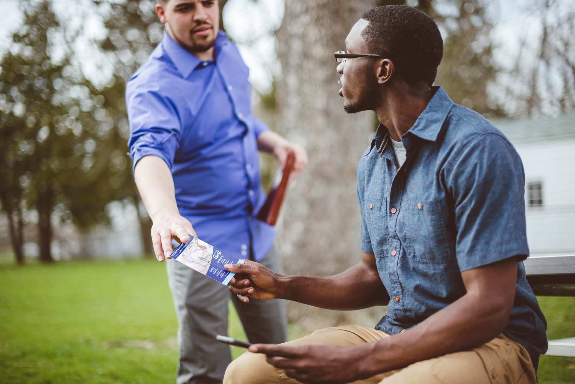 Two men are sitting on a bench in a park talking to each other.