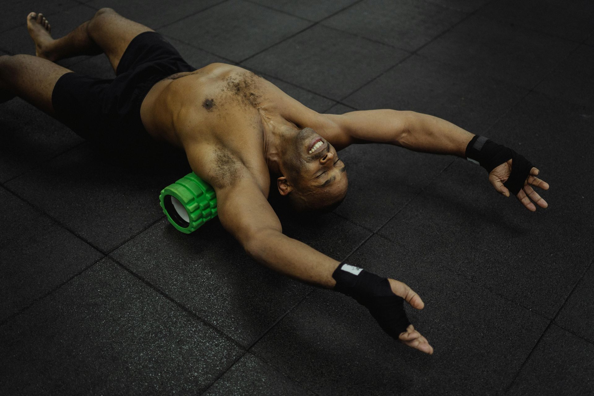 Man lying on gym floor beside a green foam roller, arms outstretched after a workout