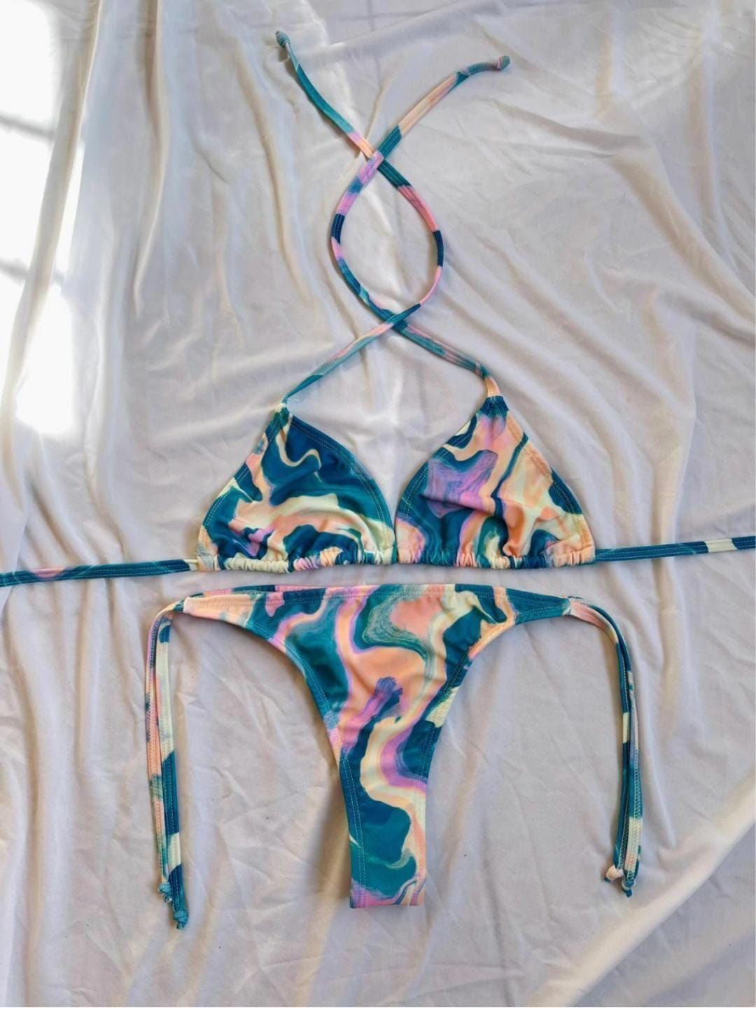 Conjunto de bikini con estampado jaspeado en tonos azules, verde azulado, morado y melocotón sobre un fondo de tela blanca.