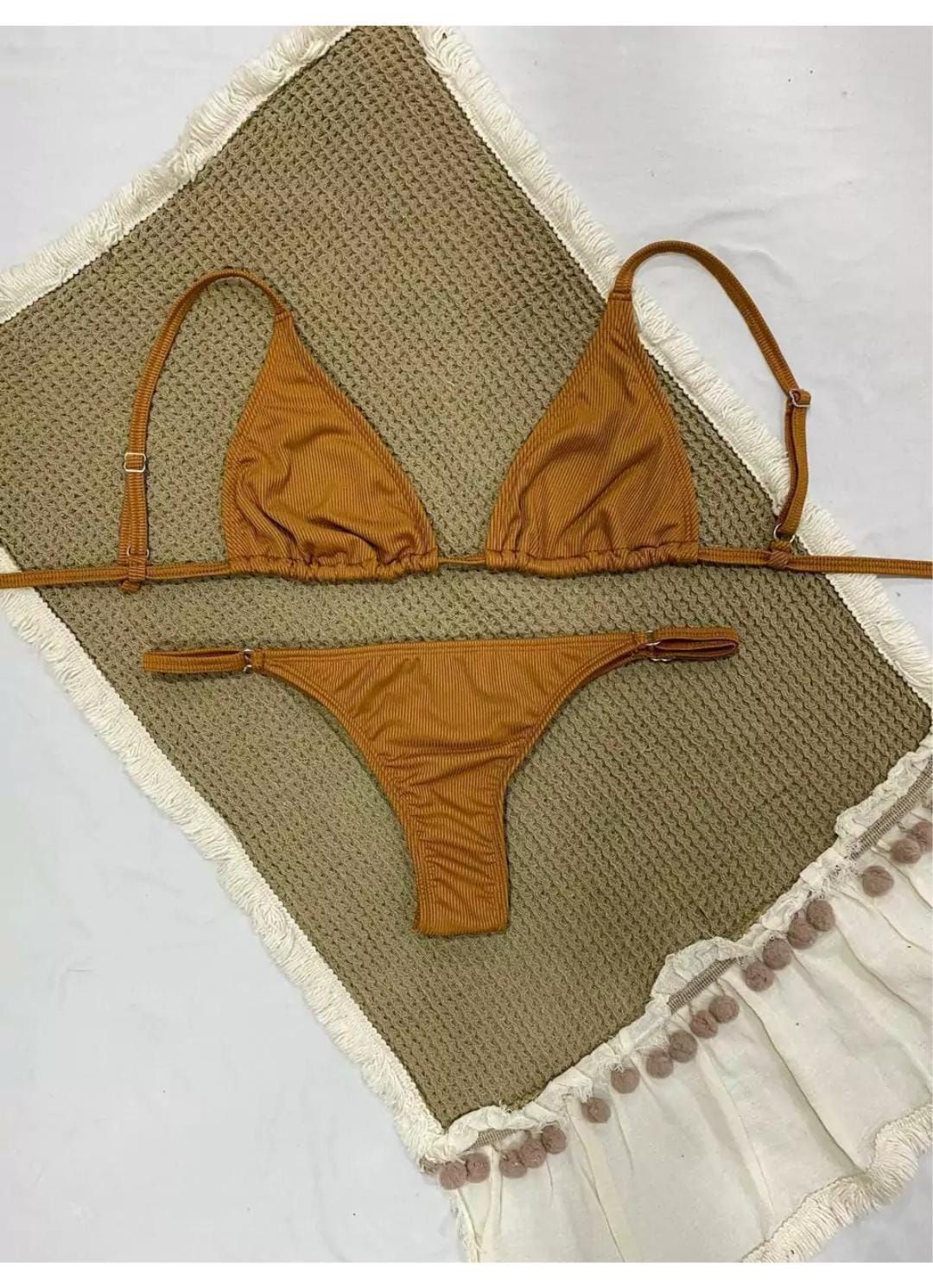 Bikini marrón sobre un mantel texturizado de color canela con ribetes blancos y pompones.