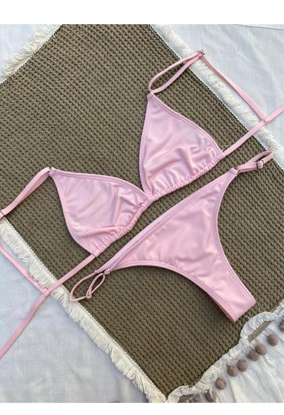 Conjunto de bikini rosa sobre tapete tejido marrón con ribete en color claro.