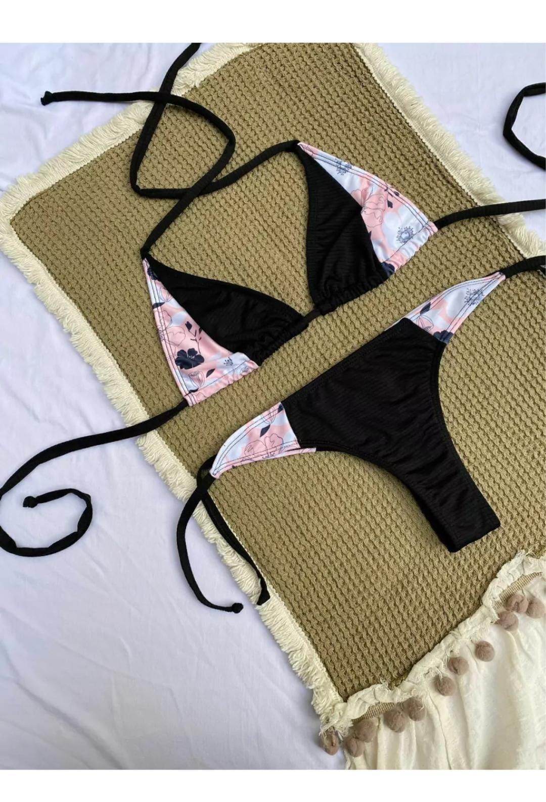 Bikini negro con paneles con estampado floral sobre una manta texturizada de color bronce.