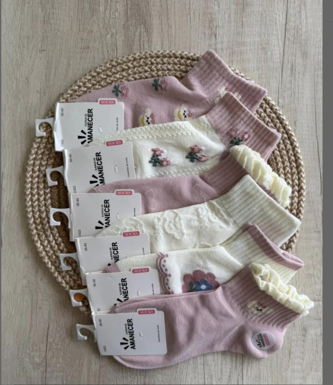 Seis pares de calcetines tobilleros estampados en color rosa y blanco sobre una alfombra tejida, cada uno con una etiqueta.