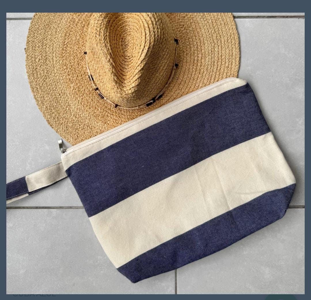 Clutch de rayas azules y blancas con sombrero de paja sobre superficie de azulejo.