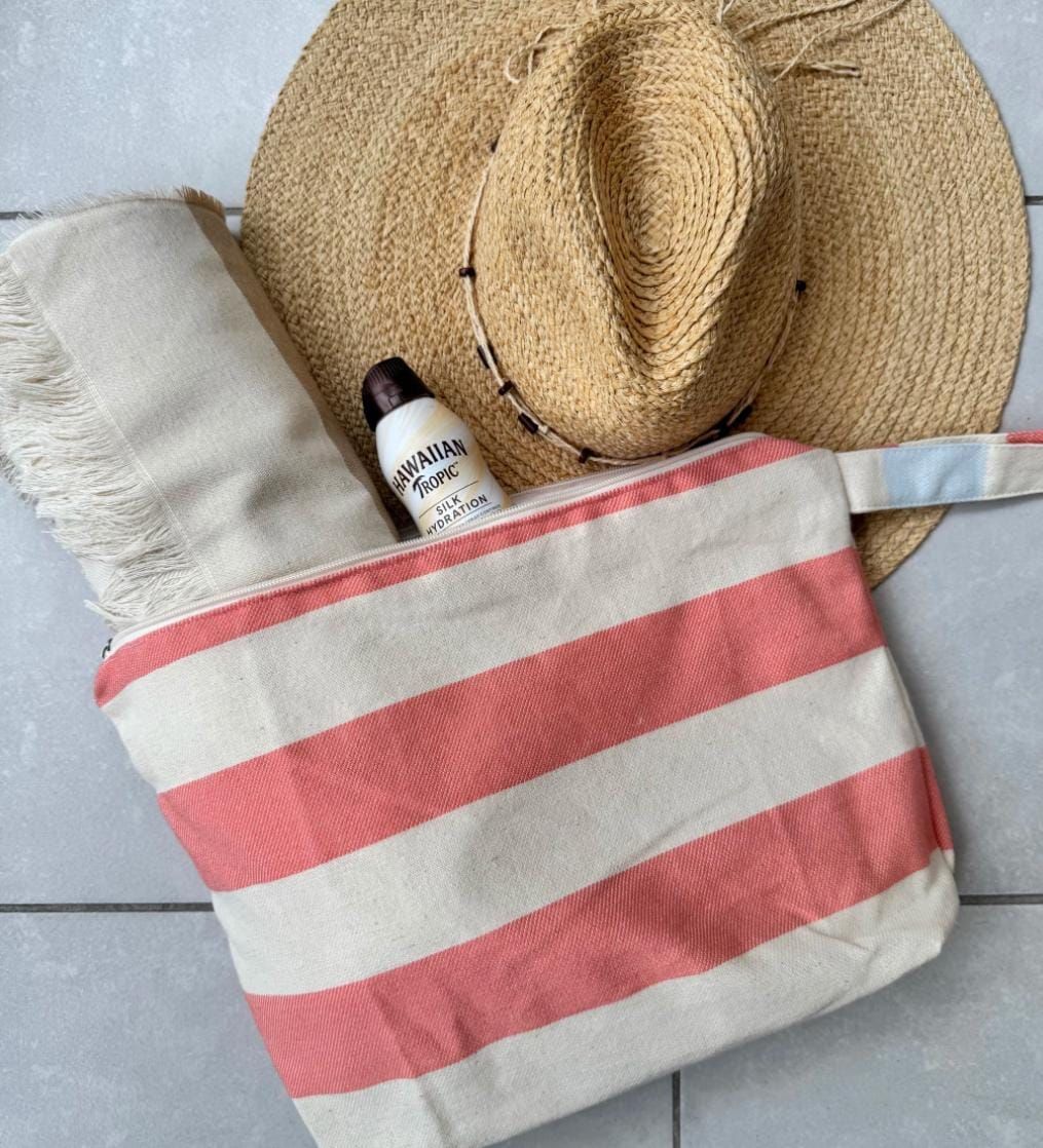 Sombrero de paja, bolso de playa con rayas rojas, protector solar y toalla de playa.