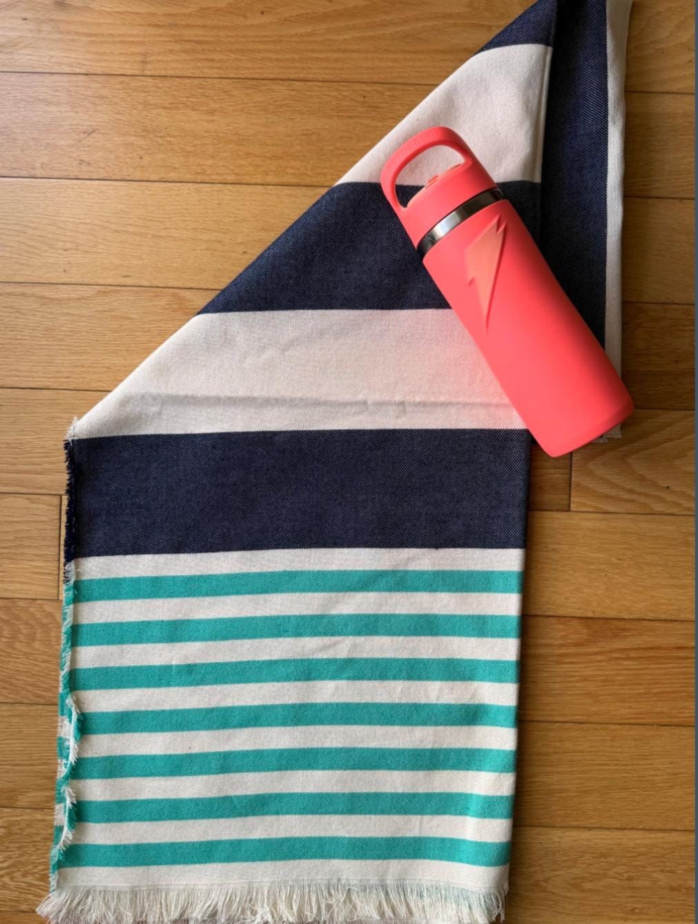 Toalla de rayas con botella de agua rosa sobre un suelo de madera.