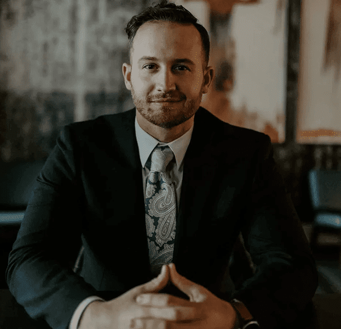 Man in blue suit, red tie, smiling; studio shot.